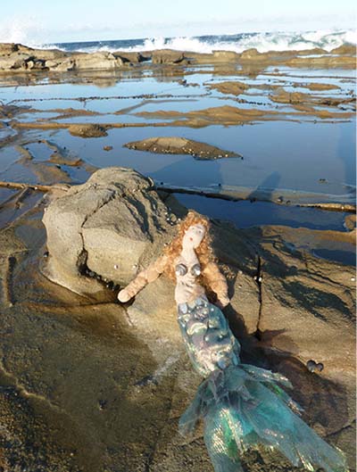 Image of mermaid doll in sand at beach