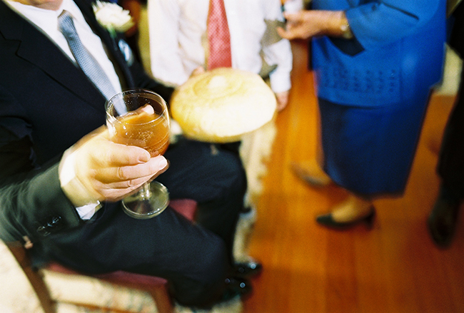 Photo of a person at a sitting in the middle of other people holding a drink and a bread. 