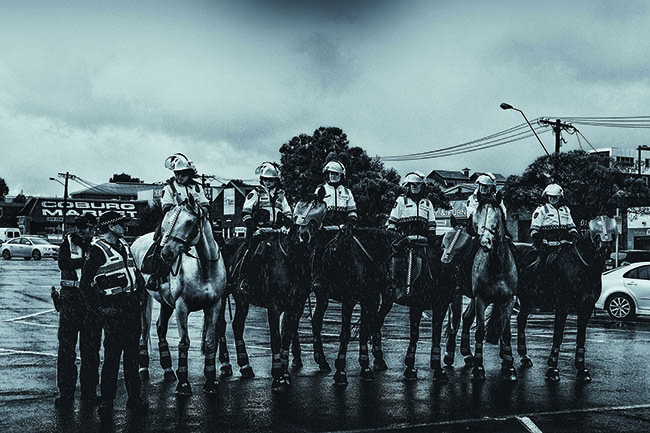 Black and white photo of mounted police in street.